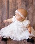 Model baby girl wearing special occasion white dress with black socks and black satin bows
